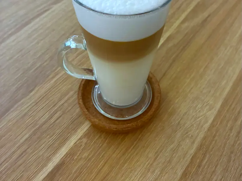 Latte aukštoje stiklinėje ant medinio stalo