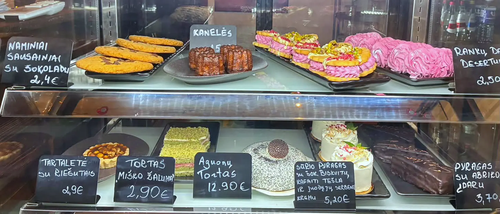 Desertų vitrina su naminiais pyragais ir kreidinėmis kainų lentelėmis